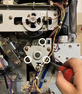 Loosening the 3 screws in the paper feed clutch base (marked in white).